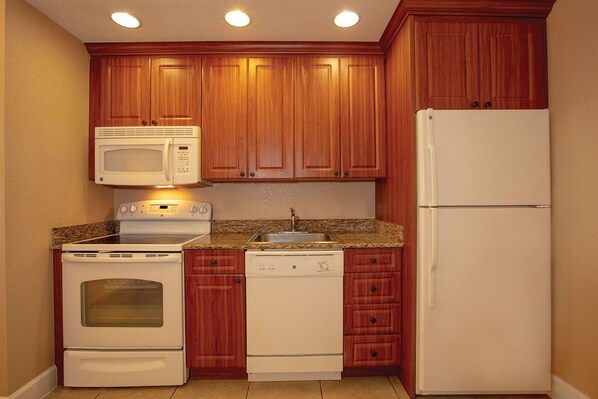 A compact kitchen with wooden cabinets, a microwave, a stove, a dishwasher, and a refrigerator.