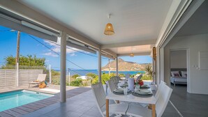 A dining area with a table set for four, overlooking a swimming pool and a scenic view of the sea and hills. - Villa Macaré - Two Bedroom Villa, Sleeps 5 (Le Marin)