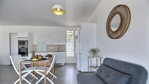 A modern kitchen with white cabinets, a dining area with a wooden table and chairs, and a grey sofa. - Villa Macaré - Two Bedroom Villa, Sleeps 5 (Le Marin)