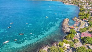 An aerial view of a coastal town with clear blue waters, boats, and a mountainous backdrop. - Villa Macaré - Two Bedroom Villa, Sleeps 5 (Le Marin)