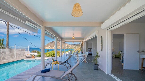 A covered outdoor area with a pool, lounge chairs, and a view of the sea. - Villa Macaré - Two Bedroom Villa, Sleeps 5 (Le Marin)