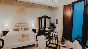 A bedroom with a large bed, a sitting area with a sofa and chairs, a small table with a plant, and a large window with a view. - Los Murmullos Casa Boutique Campeche (Campeche)