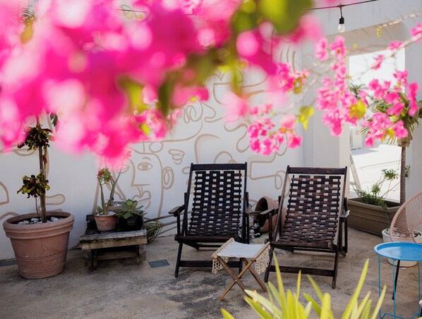 A patio area with two wooden chairs, potted plants, and a wall with a face mural. - Los Murmullos Casa Boutique Campeche (Campeche)