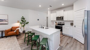 A modern kitchen with white cabinets, a central island with stools, a microwave, and a refrigerator. - WindMark | Golf Cart | Pet Friendly | In-Law Suite (Port St Joe)