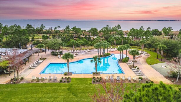 A swimming pool with lounge chairs, surrounded by greenery and a view of the ocean at sunset. - WindMark | Golf Cart | Pet Friendly | In-Law Suite (Port St Joe)