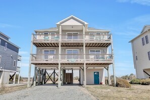 Een meerhoog gebouw aan het strand met balkons, een overdekte ingang en een blauwe deur.