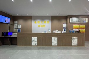 Un mostrador de recepción de hotel con una pantalla digital, un cartel de bienvenida enmarcado y carteles informativos en la pared.