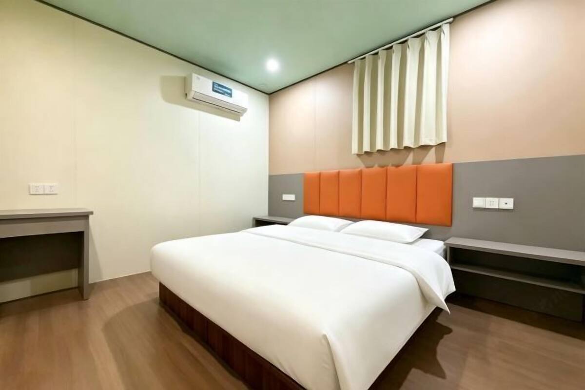 Une chambre d’hôtel équipée d’un lit, d’un bureau, d’une chaise, d’une fenêtre avec des rideaux et d’un appareil de climatisation.
