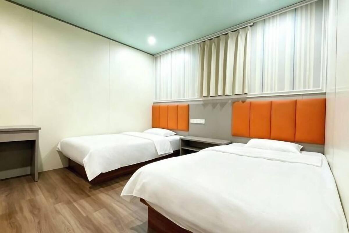 Une chambre d’hôtel avec deux lits, un bureau et une fenêtre avec des rideaux.