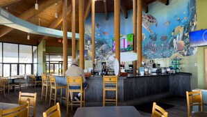 A restaurant with a high ceiling, wooden beams, and a mural of marine life on the wall.