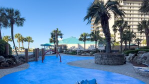 A pool area with a blue surface, palm trees, and a building in the background.