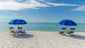 A beach with two blue umbrellas and four beach chairs.