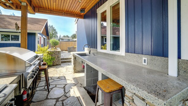 Ett utomhuskök med grill, barstolar och en stenlagd uteplats.