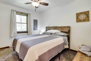 Un dormitorio con cama, ventilador de techo, ventana con cortinas, interruptor de luz en la pared y decoración de pared con temática de brújula.