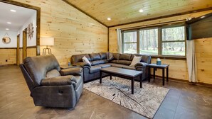 A log cabin interior with a leather sofa, a coffee table, and a view of the forest through large windows. - Near Memorial Park: Lake Arbutus Vacation Rental (Hatfield)