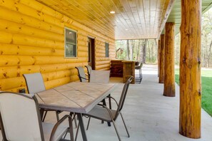 Una cabaña de troncos con comedor que incluye una mesa y sillas, una terraza de madera y vistas al bosque circundante.