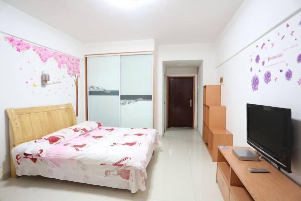 A bedroom with a bed, a TV, a wardrobe, and a door leading to another room.
