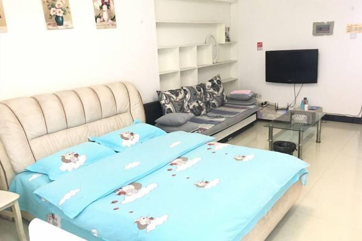 A bedroom with a bed, a sofa, a TV, and a small table.