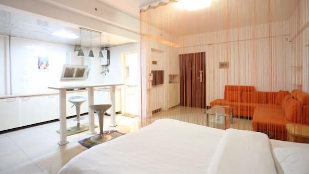 Ein Hotelzimmer mit Bett, Schreibtisch mit Stuhl, kleinem Tisch, einer orangefarbenen Couch und einer Vorhangwand.
