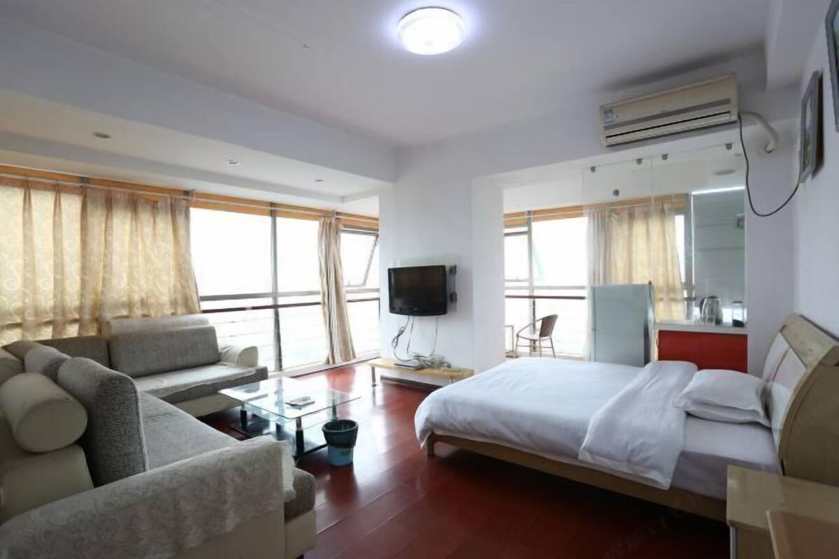 A hotel room with a bed, sofa, TV, desk, and large windows.
