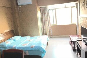 Ein Hotelzimmer mit Bett, Schreibtisch, Stuhl, einem Fenster mit Vorhängen und einer Wandklimaanlage.