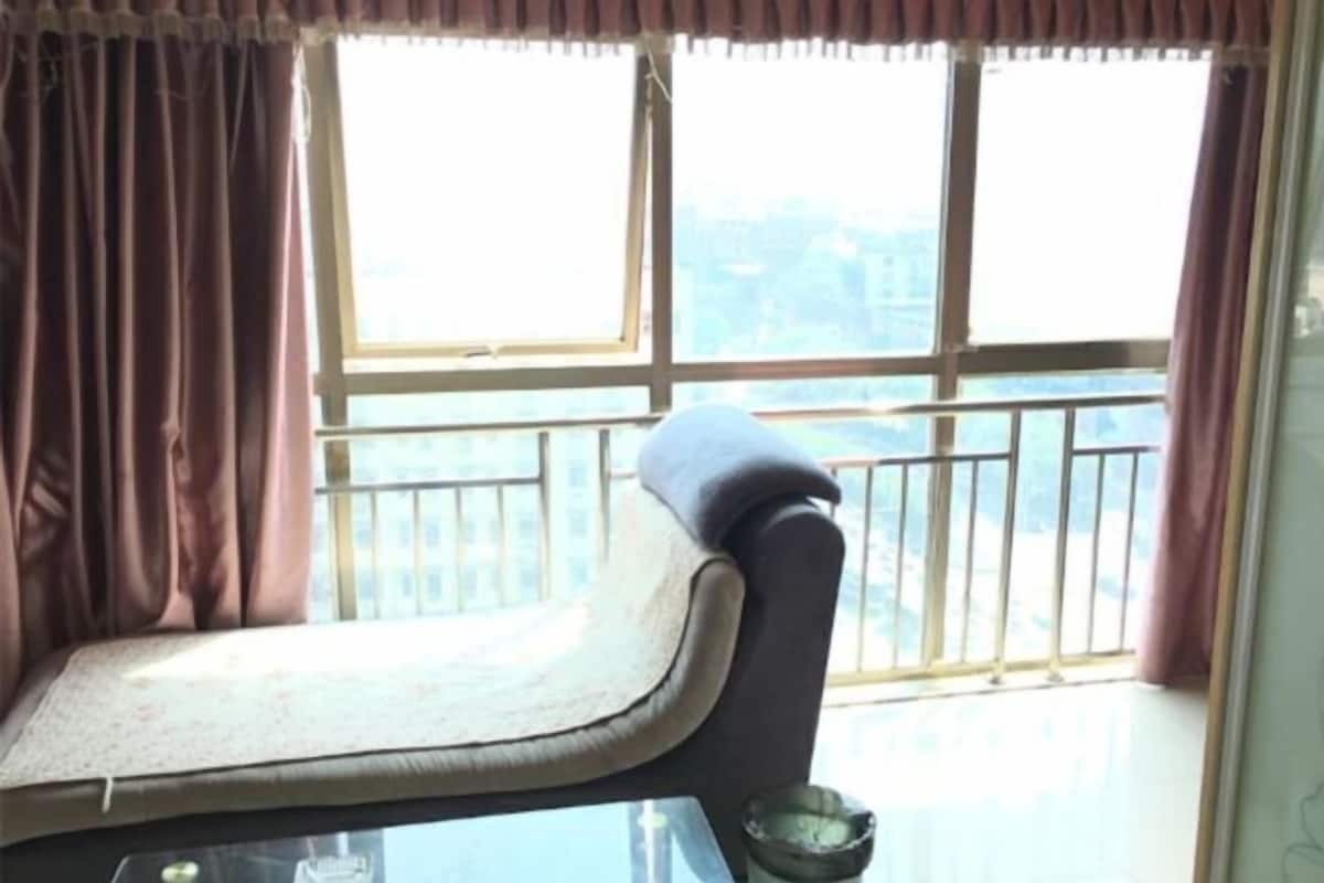 A room with a sofa facing a large window with a view of buildings.