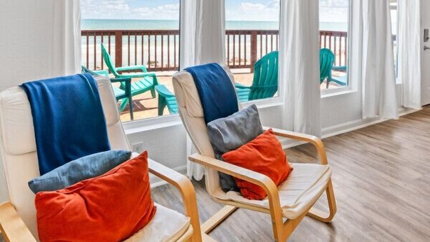 Una habitación con dos sillas frente a un balcón con vista a la playa.