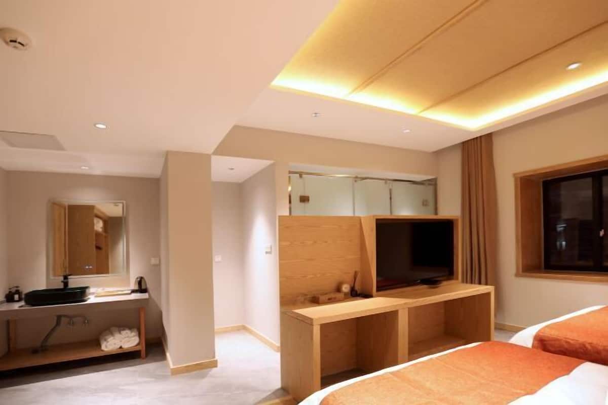 A modern hotel room with a wooden desk, a television, a large mirror, and a bed with orange bedding.