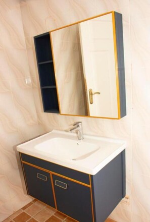 Ein Badezimmer mit einem weißen Waschbecken, einem dunkelblauen Schrank und einem Spiegel mit goldener Rahmung.
