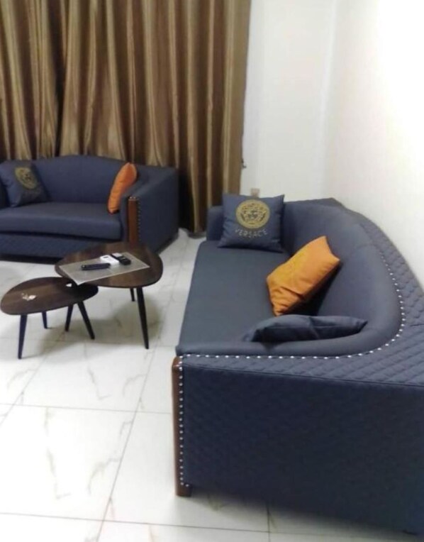 Ein Wohnzimmer mit einem dunkelblauen Sofa, einem kleineren Sessel und einem Couchtisch. Auf dem Sofa liegen zwei Zierkissen.