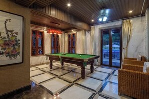 A billiards table in a room with a tiled floor, a framed artwork on the wall, and a wicker chair. - Ningxiang Shande Hall Inn (Ningxiang)