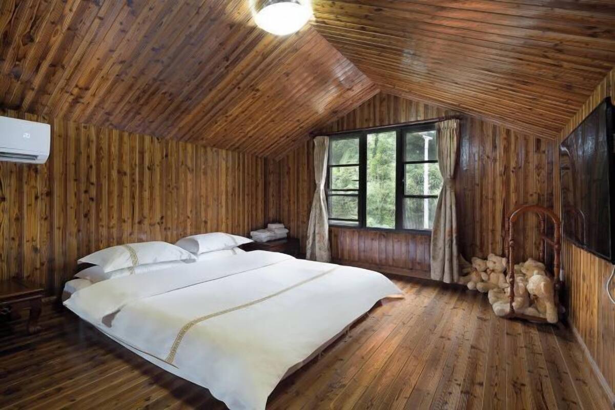 Une chambre dans une cabane en bois, avec un lit, une fenêtre et un climatiseur fixé au mur.