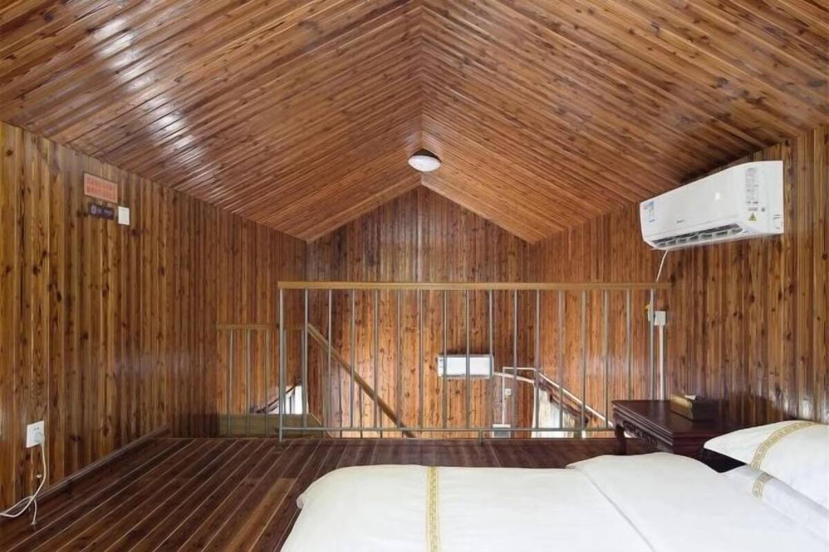 Une pièce aux murs en bois et au plafond en pente, comprenant deux lits, un bureau et un climatiseur fixé au mur.