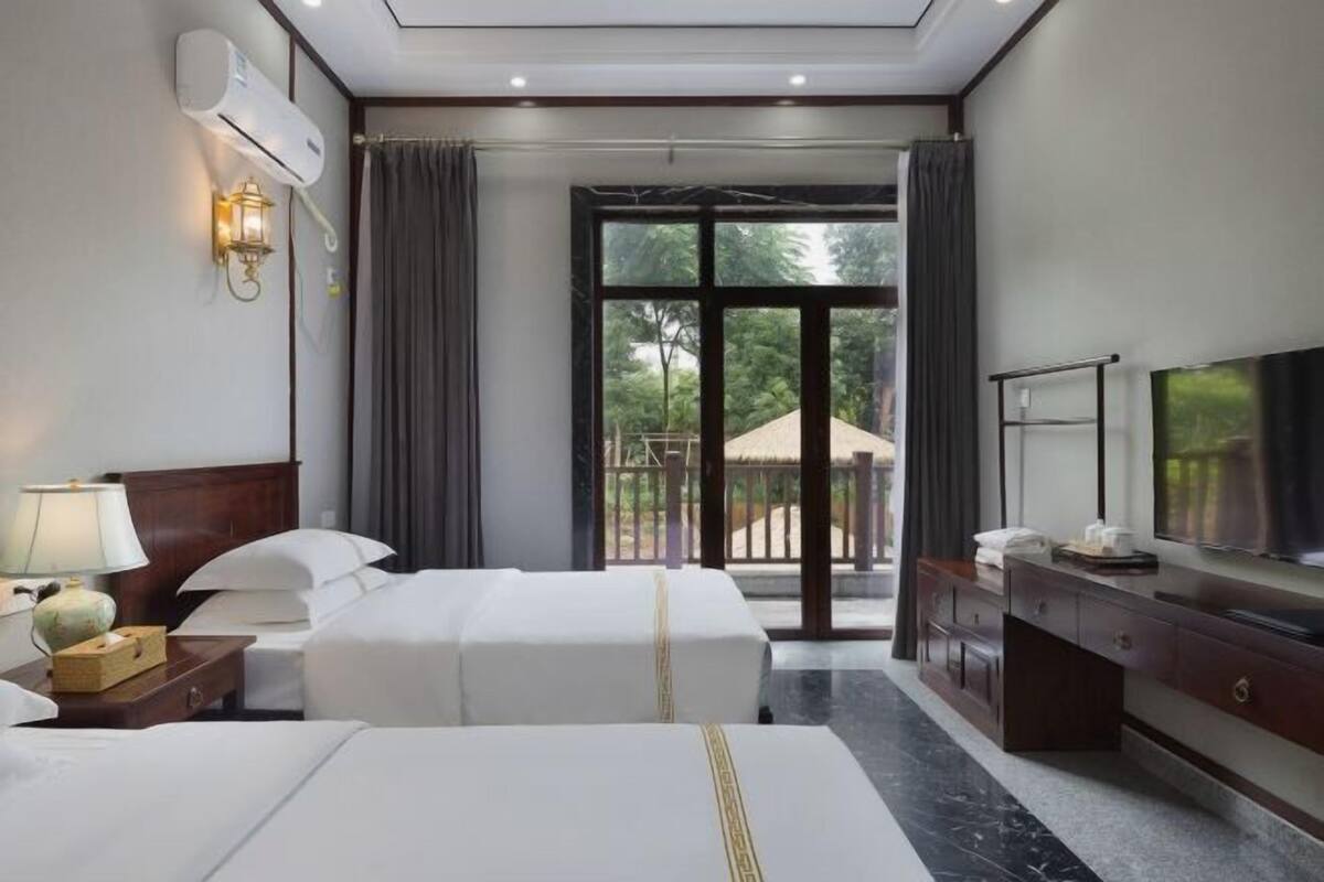 Une chambre d’hôtel avec deux lits, une télévision, un bureau, une lampe et une vue sur l’extérieur.