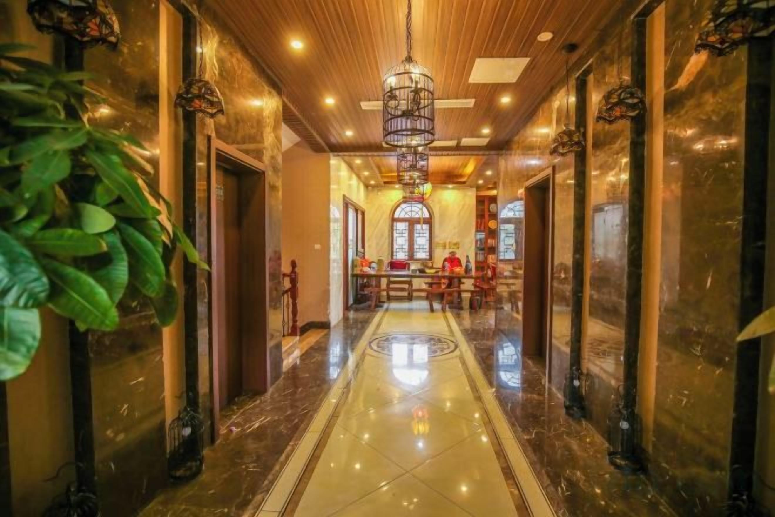 Un vestíbulo de hotel con piso de mármol pulido, una lámpara de araña central y un mostrador de recepción.