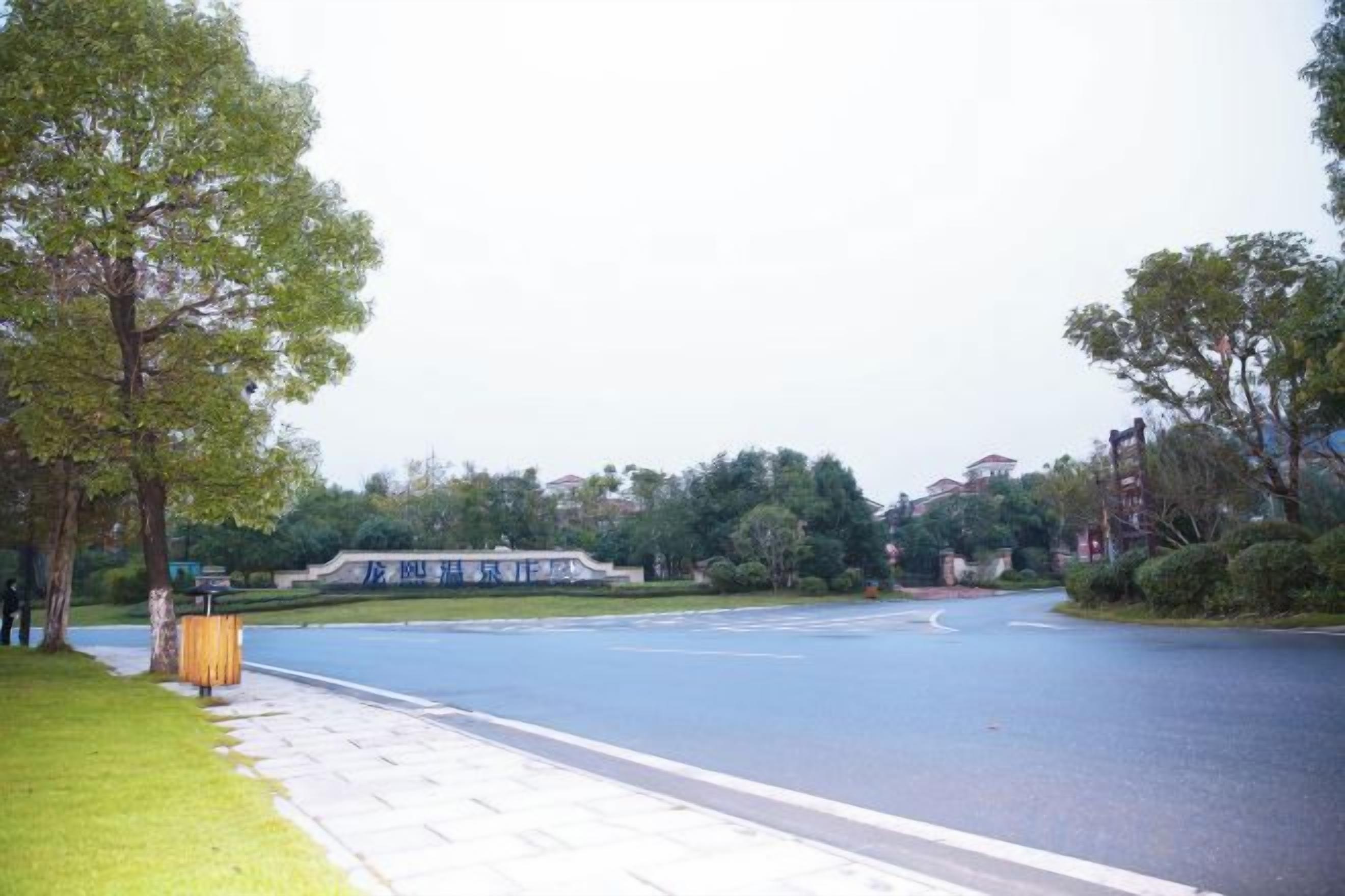 A paved walkway alongside a road with trees and a building in the background.