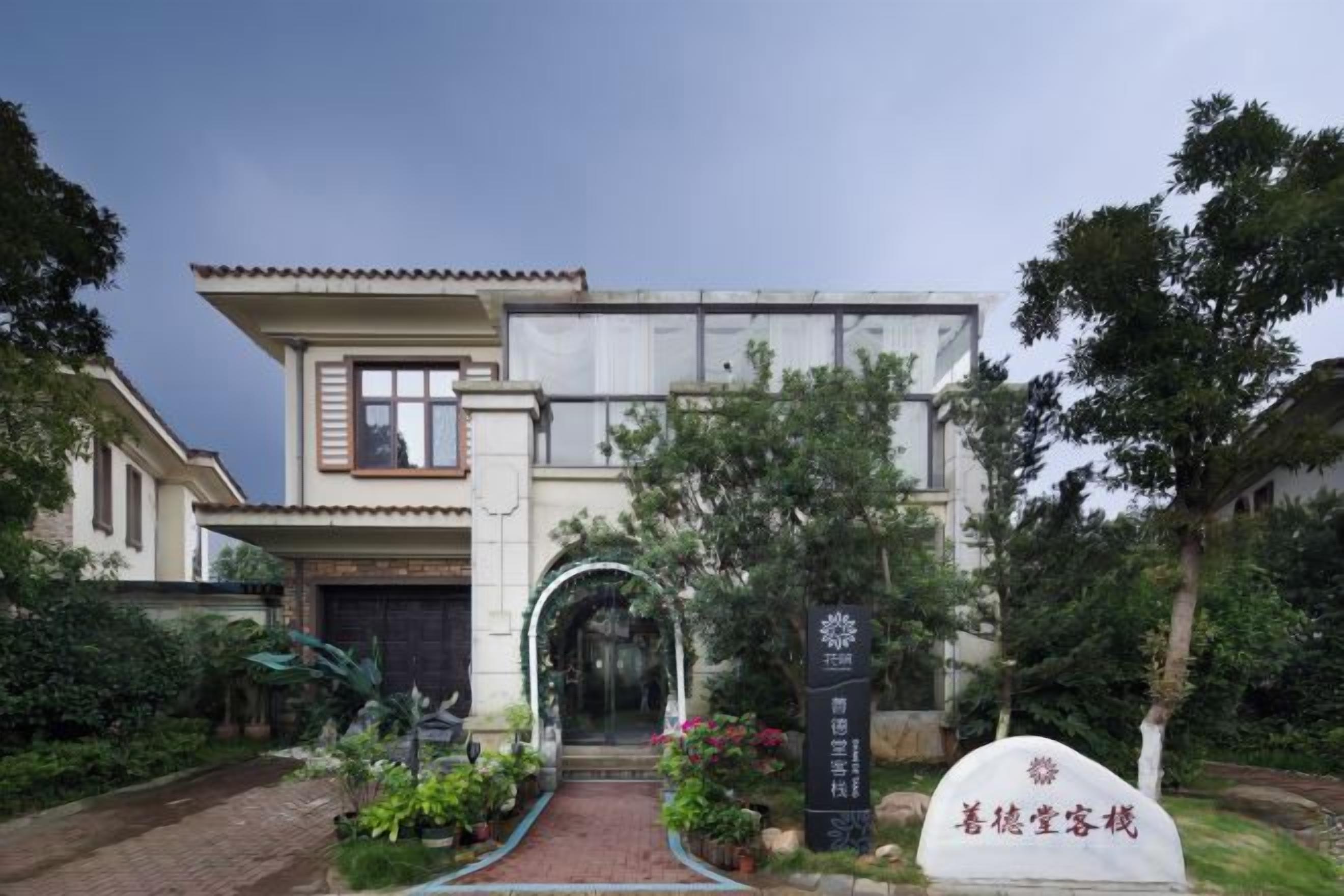 Un edificio tradicional con entrada central, rodeado por un jardín con diversas plantas y un camino que lleva a la puerta.