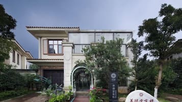 Un edificio tradicional con entrada central, rodeado por un jardín con diversas plantas y un camino que lleva a la puerta.