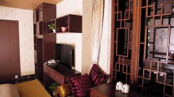 Una habitación con cama, escritorio con computadora, televisor y ventana con cortinas.