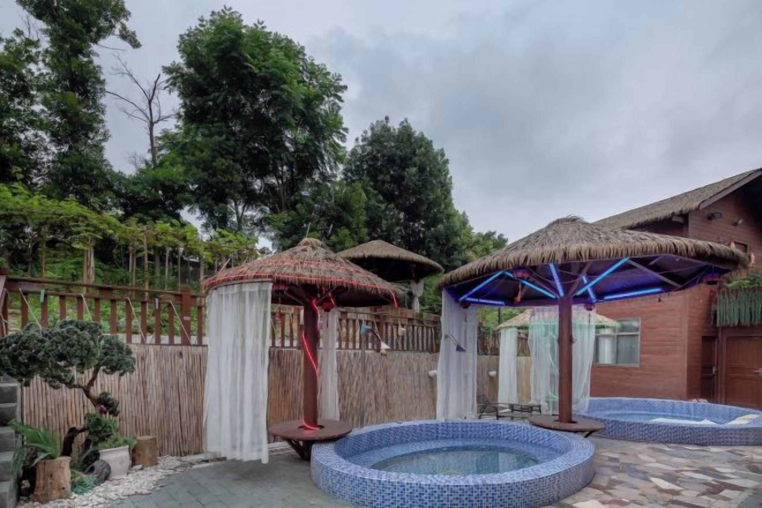 A backyard with a hot tub, two thatched-roof structures, and a wooden fence.