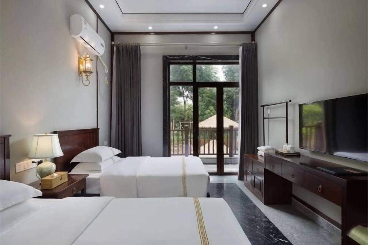 Une chambre d’hôtel avec deux lits, une télévision, un bureau et une grande fenêtre donnant sur un paysage verdoyant.