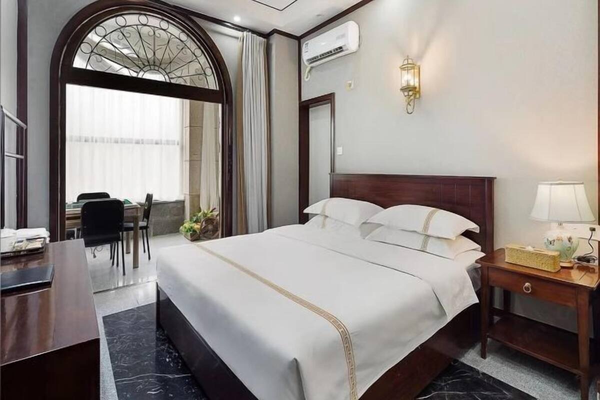 Une chambre d’hôtel avec un grand lit, un bureau, une chaise, un appareil de climatisation, une lampe et un miroir décoratif.