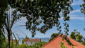 Une maison avec un toit recouvert de tuiles rouges, entourée d’une végétation luxuriante et offrant une vue dégagée sur la mer.