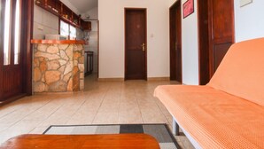 Un salon avec une cheminée en pierre, une cuisine à l’arrière-plan et une porte en bois.