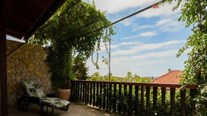 Un espace extérieur abrité, doté d’un mur en pierre, d’un fauteuil de relaxation, d’une grande plante en pot et d’une clôture en bois.