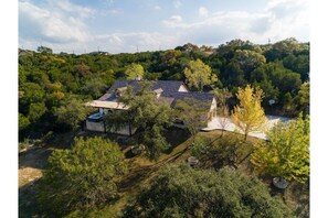 Une maison entourée d’une forêt dense, sous un ciel dégagé.