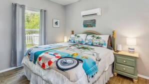 A bedroom with a bed, a nightstand, a lamp, an air conditioner, and a window with curtains. - Castaway Tiny Home in Bon Secour near Bon Secour River, 8 miles to sportsplex (Bon Secour)