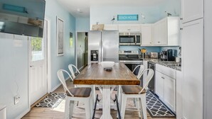A compact kitchen with white cabinets, a wooden dining table, and a sign reading "BEACH HOUSE". - Castaway Tiny Home in Bon Secour near Bon Secour River, 8 miles to sportsplex (Bon Secour)