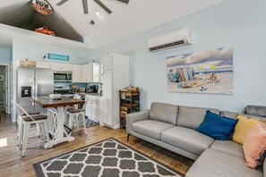 Cozinha moderna com armários brancos, uma mesa de jantar com cadeiras e um sofá cinza com almofadas coloridas.