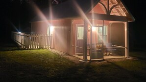 A small, single-story building with a sloped roof, a porch, and a fenced area. - Castaway Tiny Home in Bon Secour near Bon Secour River, 8 miles to sportsplex (Bon Secour)
